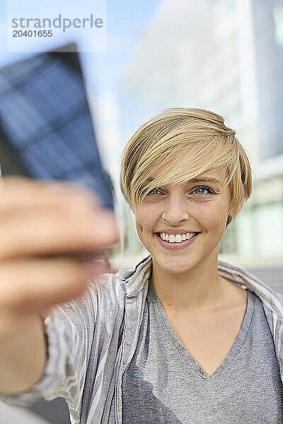 Smiling blond young woman taking selfie through smart phone