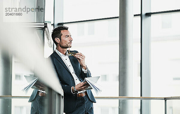 Businessman holding documents and leaning on railing at office