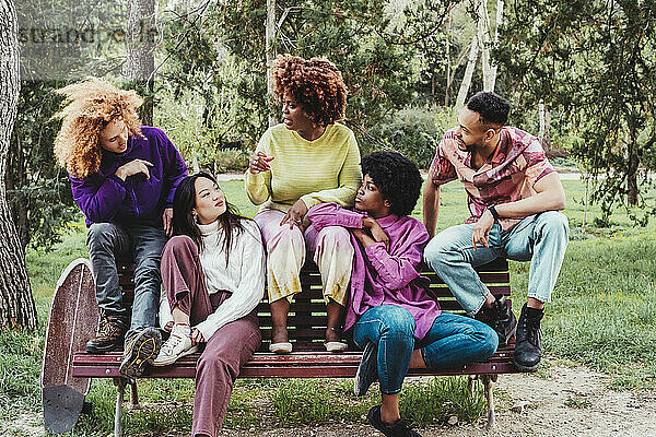 Multiracial friends talking with each other sitting on bench at park