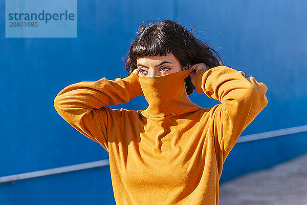 Young woman covering face with orange colored turtleneck