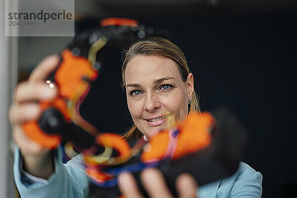 Smiling mature engineer examining robotic arm at office