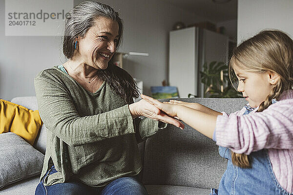 Happy granddaughter and grandmother sitting on sofa at home