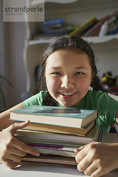 Smiling girl with stack of books at home