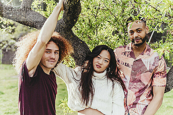 Smiling multiracial friends standing near tree at park