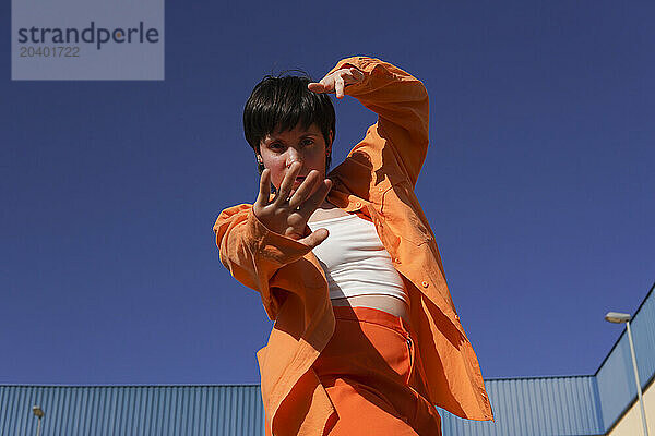 Confident woman in orange casuals dancing under clear blue sky on sunny day