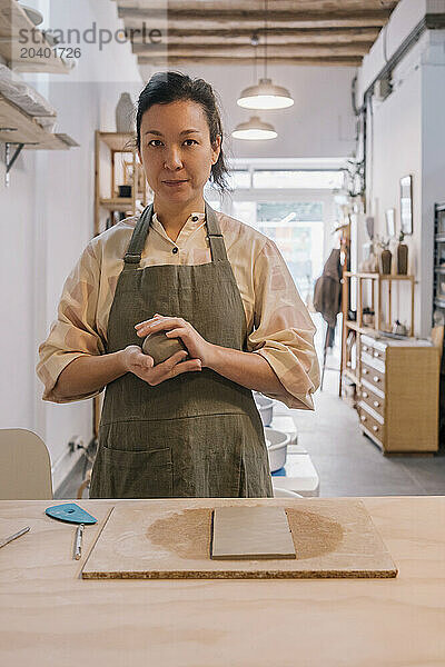 Skilled craftsperson molding clay standing by table at pottery workplace