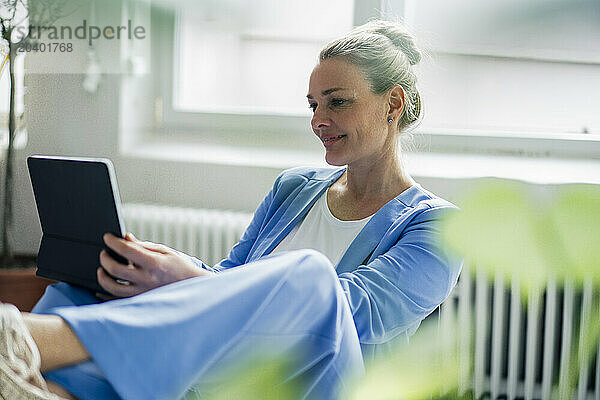 Smiling mature businesswoman using tablet PC sitting in office