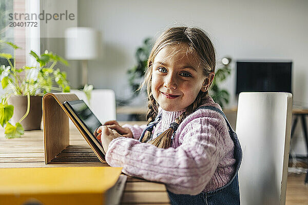 Smiling girl sitting with tablet PC at table at home