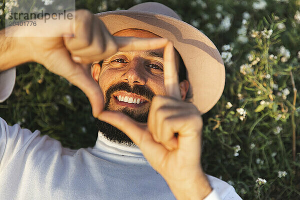 Happy man looking through finger frame in front of flowering plants