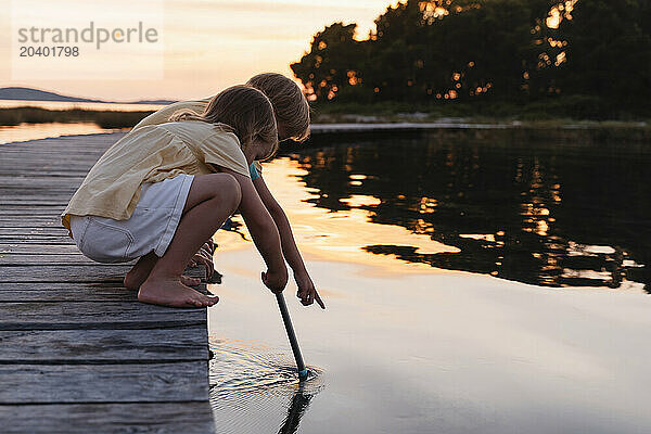 Brother and sister crouching on pier with fishing net in lake at sunrise