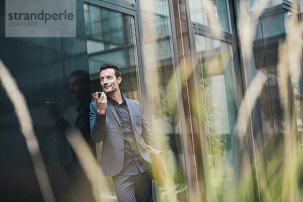 Businessman talking through speaker phone near office building