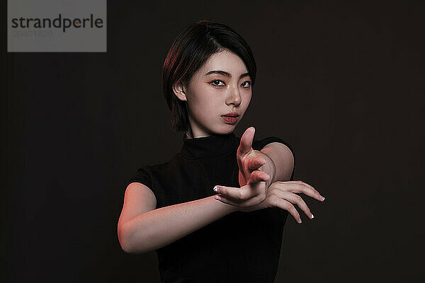 Young woman making shoot gesture against black background