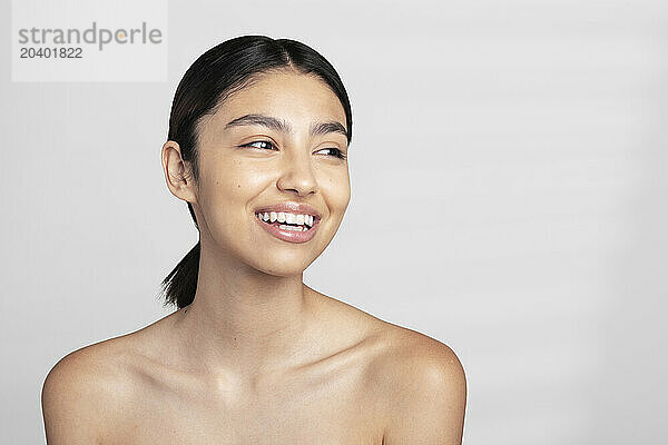 Happy beautiful young shirtless woman looking away against white background