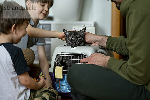 Father and sons with cat in cage at home