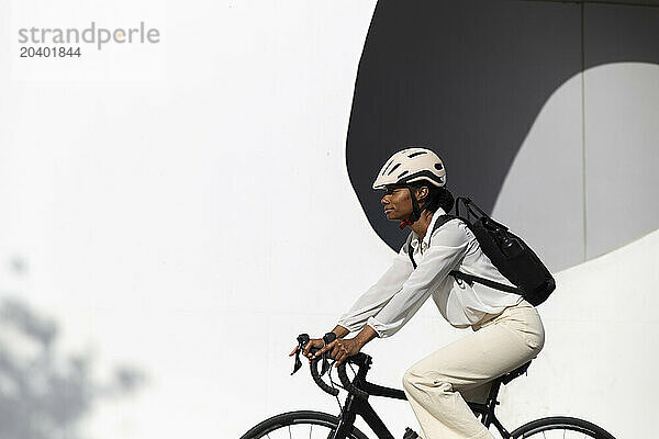 Businesswoman cycling bicycle by white building