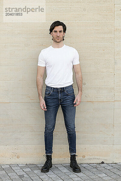 Confident young man standing in front of beige wall