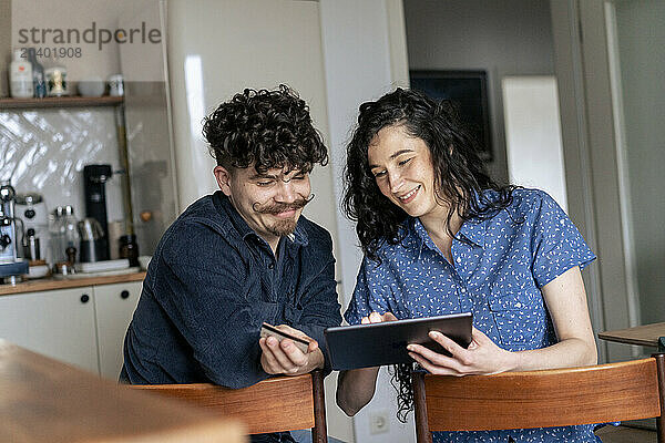 Smiling woman sharing tablet PC with man on chair at home