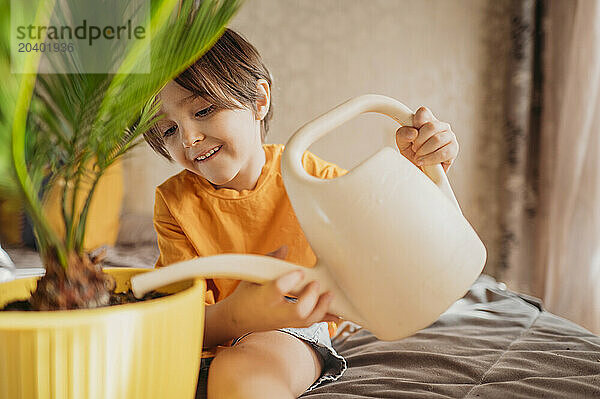 Happy boy watering potted plant with in bedroom at home