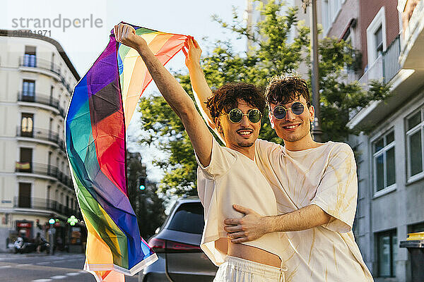 Happy young couple waving rainbow flag at gay pride parade