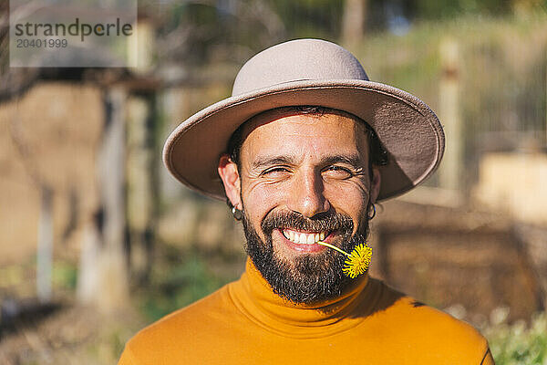 Happy man wearing hat and holding flower with teeth