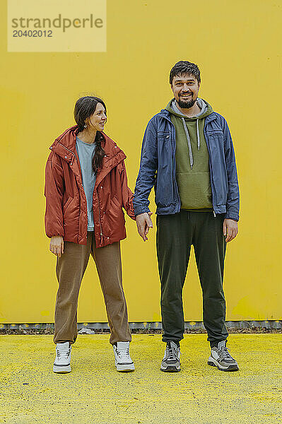 Happy couple holding hands and standing in front of yellow background