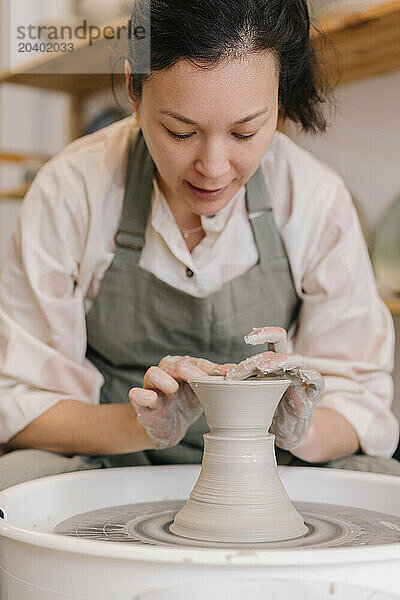 Confident craftsperson molding clay on pottery wheel at workplace