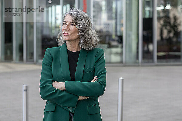 Thoughtful senior businesswoman with arms crossed standing on footpath