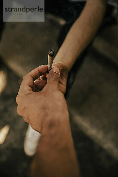 Hand of man passing marijuana joint to friend