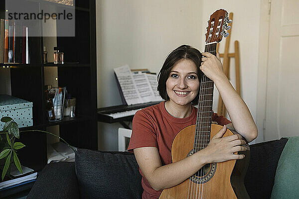 Happy beautiful woman with guitar sitting at home