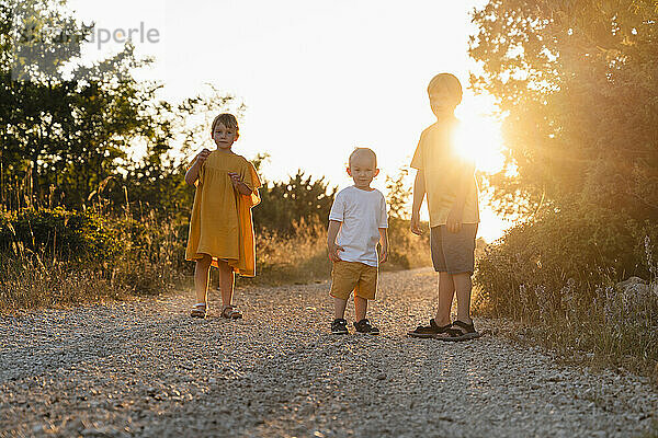 Back lit siblings standing on footpath at sunset