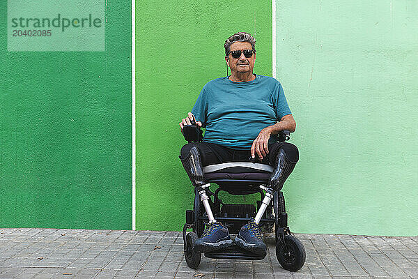 Senior man in motorized wheelchair in front of green wall