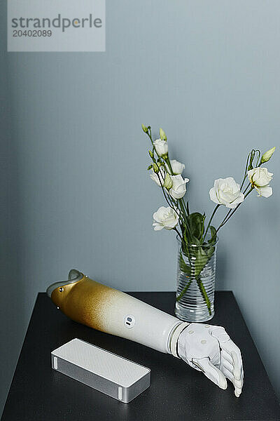 Prosthetic arm and vase with white roses on night table in bedroom at home