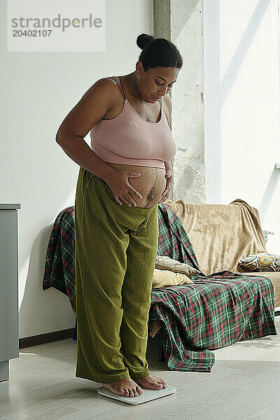 Plus size pregnant woman standing on scale at home