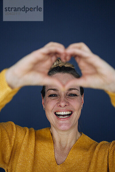 Happy beautiful woman showing heart shape against colored background