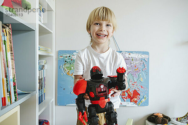 Smiling boy holding robot while standing in room at home