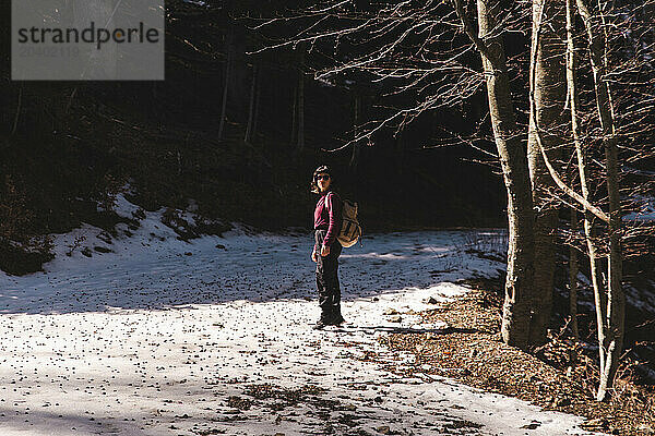 Young woman standing on snowy pathway at forest