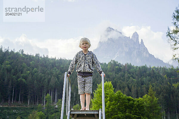 Blond boy standing on top of slide at playground