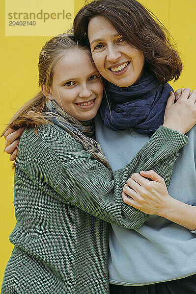 Smiling woman embracing daughter against yellow background