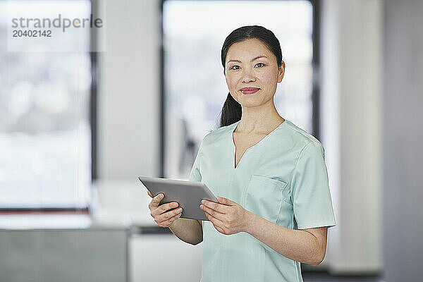 Portrait of nurse in scrubs holding digital tablet