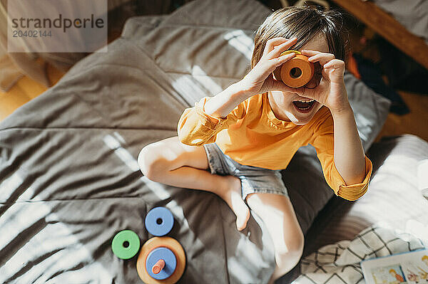 Playful boy looking through toy sitting on bed at home