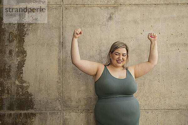 Cheerful curvy woman flexing muscles in front of wall