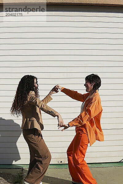 Happy lesbians holding hands dancing together in front of white wall