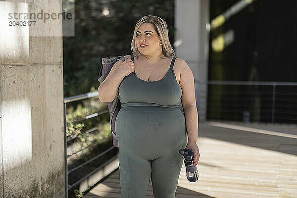 Curvy young woman with water bottle standing on footbridge