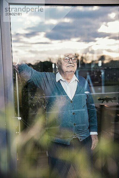 Thoughtful senior man looking out through window