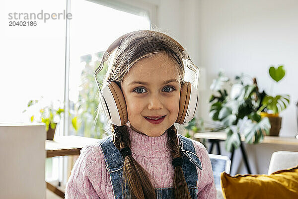 Smiling girl listening to music through wireless headphones at home