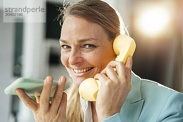 Happy businesswoman talking through mobile phone and telephone at office