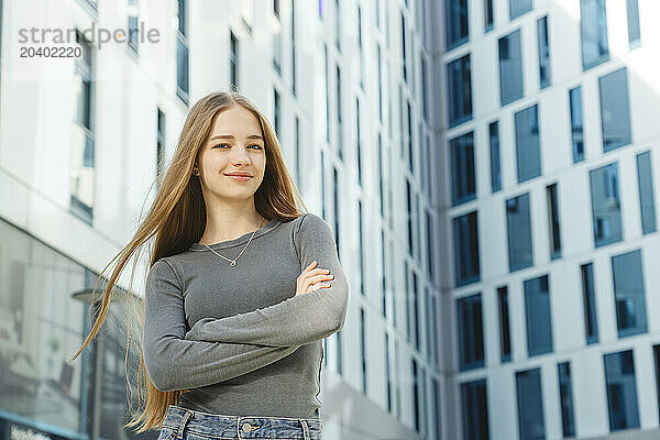 Confident teenage girl with arms crossed in front of building