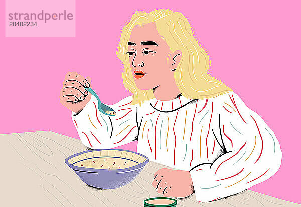 Woman enjoying soup with blue spoon at table in front of pink background