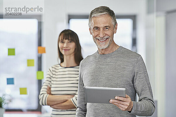 Smiling businessman holding tablet computer with colleague at workplace