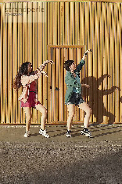 Happy gay couple dancing together in front of brown building wall